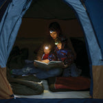 A camping family reading in a tent wearing head torches